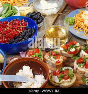 Abwechslungsreiche Snacks auf dem Esstisch, Wein, Nudeln und bruschettes mit Avocado und Tomaten Clos Stockfoto