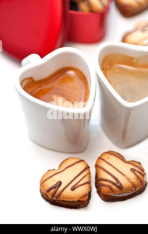 herzförmige Creme Cookies auf rotes Herz Metallbox und paar Espresso Kaffeetassen Stockfoto