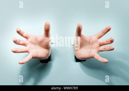 Fremde Hände kommen durch Löcher in einem blauen Karton. Stockfoto