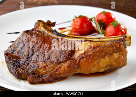 Club-Steak. Kalbfleisch auf den Knochen. Gegrilltes Fleisch Rippen auf weißen Teller mit Cherry-Tomaten und dunklen hot sauce Stockfoto