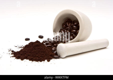 Ein Mörser mit frisch gerösteten Kaffeebohnen mit Vor einem Haufen von kaffeepulver; auf einem weißen Hintergrund verschüttet Stockfoto