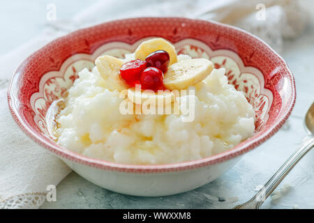 Schüssel mit Milch Reisbrei, Bananen, Beeren und Honig. Stockfoto