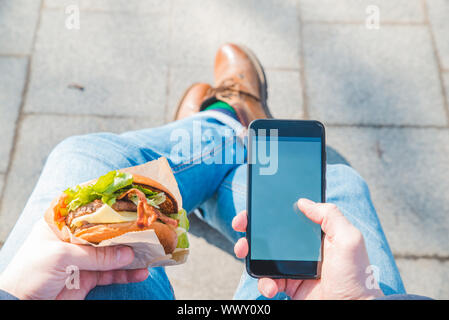 Mann hält Burger und Handy. weißer Bildschirm Stockfoto