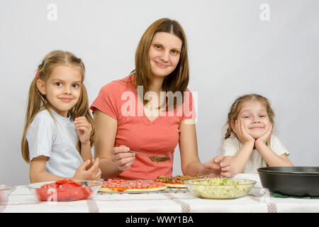 Mama mit zwei kleinen Mädchen sitzen am Küchentisch eine Pizza vorbereiten Stockfoto