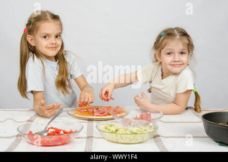 Zwei glückliche Mädchen am Tisch verteilt auf den Pizzazutaten Stockfoto