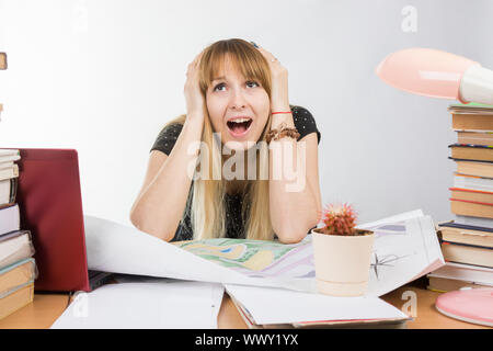 Mädchen-Design-Student an einem Schreibtisch mit einem Stapel Bücher und Projekte in ihrer Verzweiflung packte den Kopf Stockfoto