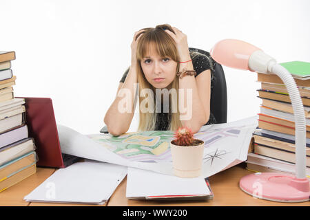 Student-Designer hinter einem Schreibtisch mit einem Stapel Bücher und Projekte sitzt mit seinem Kopf in den Händen Stockfoto