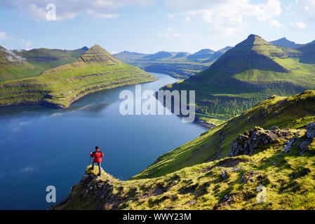 Blick auf Funningur Fjord aus dem Funningur nach oben. Eysturoy Island, Färöer Inseln. Touristen in eine rote Jacke erforscht natürlichen Attraktionen. Sommer Berg Stockfoto