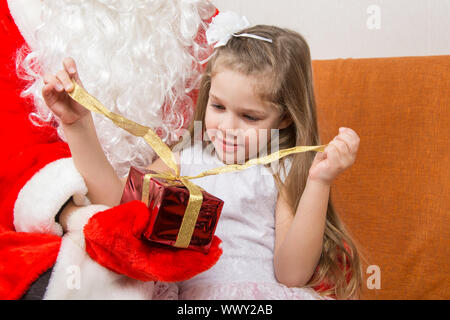 Mädchen entfesselt eine rote Schleife Geschenk in den Händen von Santa Claus Stockfoto