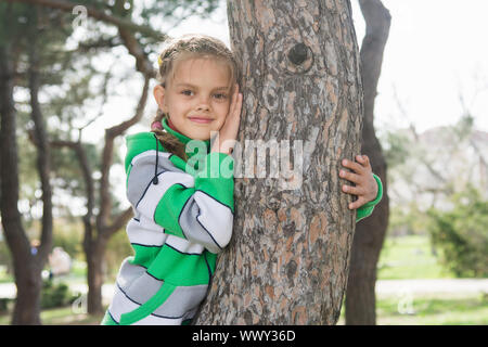 Freudige siebenjähriges Mädchen sitzen auf einem Baumstamm im zeitigen Frühjahr Stockfoto