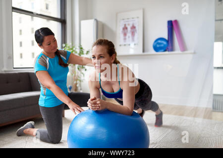 Chinesische Frau personal Trainer beim Training Training mit einer attraktiven Blondine Client in einem hellen Medizinisches Büro Stockfoto