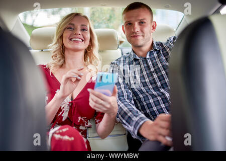 Bild der lächelnde Frau und Mann mit Handy in der Hand in den Rücksitz des Autos während der Sitzung Stockfoto