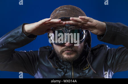 Pilot der 20s mit Sonnenbrille und Vintage aviator Helm. Trägt Lederjacke, Bart und ausdrucksvollen Gesichtern Stockfoto