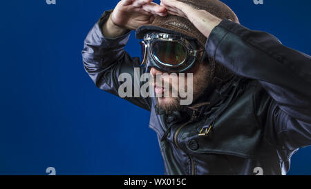 Erkunden Sie pilot Der 20s mit Sonnenbrille und Vintage aviator Helm. Trägt Lederjacke, Bart und ausdrucksvollen Gesichtern Stockfoto