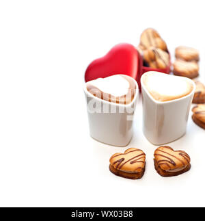 herzförmige Creme Cookies auf rotes Herz Metallbox und paar Cappuccino Kaffeetassen Stockfoto
