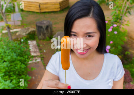 Junge asiatische Frau essen Wurst oder Hotdog, bis zu Kamera hochauflösende Bilder Galerie suchen. Stockfoto