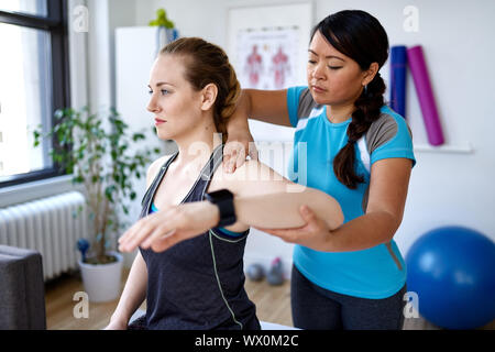 Chinesische Frau Physiotherapie Professional, eine Behandlung zu einer attraktiven Blondine Client in einem hellen Medizinisches Büro Stockfoto