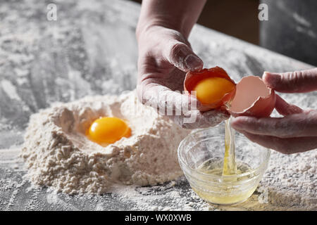 Weibliche Hände halten ein kaputtes Ei in die Hände eines Küchentisch. Konzept der Backen Stockfoto