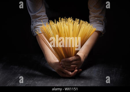 Weibliche Hände halten ungekochte spaghetti Pasta über einen hölzernen Tisch auf einem schwarzen Hintergrund. Stockfoto