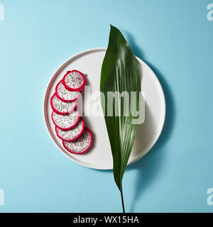 Dragon Obst oder pitaya Slice in der Platte mit grünen Blättern auf blauem Hintergrund Stockfoto