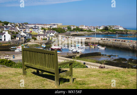 Leere Sitzbank mit Blick auf das Dorf Hafen in Cemaes Bay. Cemaes, Isle of Anglesey, Wales, Großbritannien, Großbritannien Stockfoto