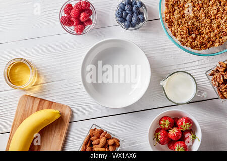 Eine Reihe von Müsli Zutaten, Bananen, Honig, Milch, Beeren und eine leere Platte für ein gesundes Frühstück. Schritt-für-Schritt kochen. Top Stockfoto