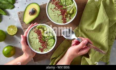 Diätetische Smoothies aus grünem Gemüse mit Flachs. Hand hält eine Frau eine Platte mit einem Smoothie und ein Löffel auf dem Hintergrund der Stockfoto