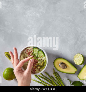 Die Hand einer Frau setzt eine Platte mit Spargel auf einem grauen konkreten Hintergrund mit einem grünen Diät Smoothie. Ansicht von oben Stockfoto