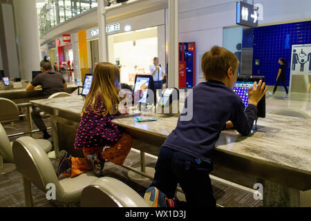 Sie Kinder spielen mit den öffentlichen Gebrauch ipads im Abflugbereich von Toronto Pearson Flughafen Stockfoto