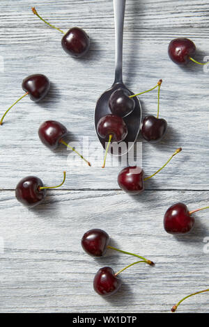 Süße Beeren Hintergrund von rot reifen Kirschen wth Löffel auf grau Holz- Hintergrund. Flach. Stockfoto