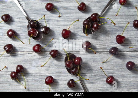 Organische bunte Kirschen Muster mit Löffeln auf hölzernen grauen Hintergrund. Stockfoto