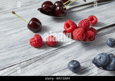 Süße berriex Mix auf grauem Hintergrund. Reifen Blaubeeren, Kirschen, Himbeeren in einem Löffel. Stockfoto