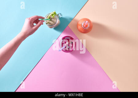 Drei farbenfrohe Smoothies in einem Glas und einer Frau Hand serviert ein trinkhalm auf farbigem Papier Hintergrund Stockfoto