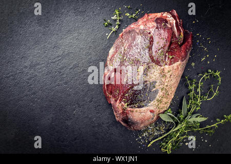 Raw trockenen Jahren rehkeule als mit Kräutern wie close-up auf einer Schiefertafel Platte mit Kopie Raum links Stockfoto