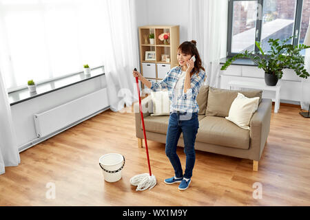Frau mit Reinigung zu Hause und auf dem Smartphone Stockfoto