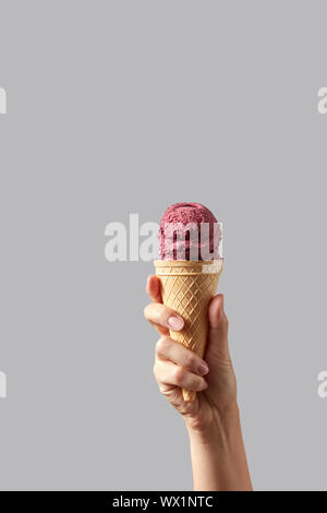 Hand hält eine Frau eine Waffel Kegel mit Red Cherry Sorbet auf einem hellgrauen Hintergrund. Stockfoto