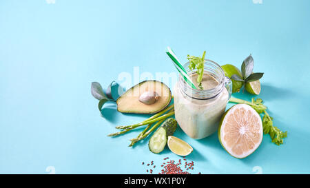 Grüne Smoothie aus biologischem Gemüse, Obst, Zitrone, Limette, Leinsamen in eine Glasschüssel auf blauem Papier Hintergrund. Stockfoto