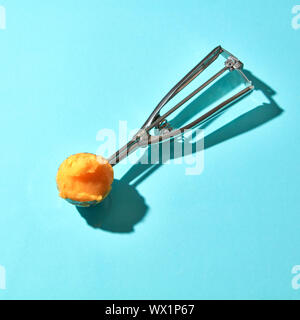 Die Löffel für Eis mit gelben mango Nachtisch auf blauem Hintergrund mit harten Schatten Stockfoto