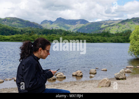 Eine junge Frau Ignorieren des Lake District auf ihr Handy, Elterwater zu konzentrieren, Großbritannien Stockfoto