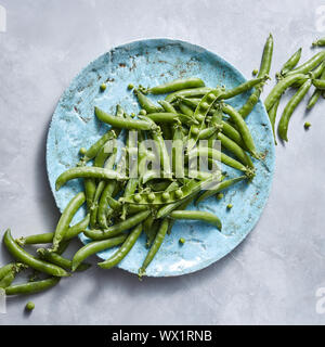 Frisch natürliche grüne Erbsen mit Stöcken auf einem blauen Keramikplatte abgeholt auf grauem Marmor Hintergrund. Stockfoto