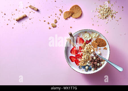 Eine weiße Schale mit organischen Joghurt Smoothie mit Erdbeeren, Banane, Blaubeere, Haferflocken und Kekse auf rosa Hintergrund. Flat l Stockfoto