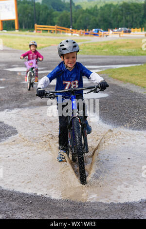 Ein Junge (7 Jahre alt), sein Fahrrad durch eine Pfütze Stockfoto