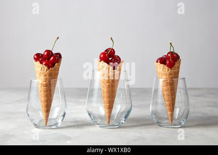 Drei Waffeln mit frischen reifen Kirschen in Gläsern auf grauem Marmor tisch. Stockfoto