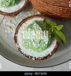 Nahaufnahme einer Hälfte der Kokosnuss mit grüner Minze Eis mit Zweig Minze und Kokos Chips. Stockfoto