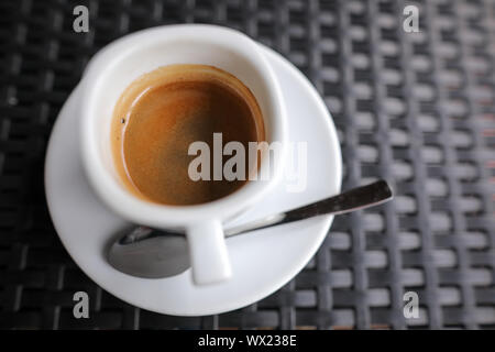 Details mit einem weißen Keramik Tasse Kaffee und eine Edelstahl Löffel auf eine Tabelle in einem Coffee Shop Stockfoto