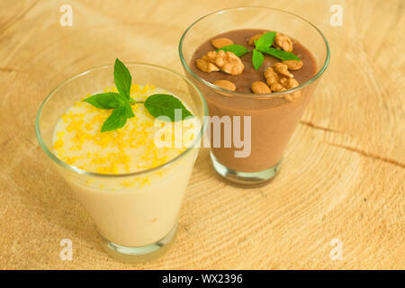 Dessert Schokoladenpudding mit Muttern und Vanillepudding mit Zitronenschale auf einem Holztisch. Stockfoto