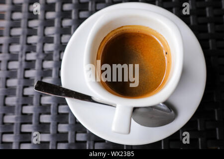 Details mit einem weißen Keramik Tasse Kaffee und eine Edelstahl Löffel auf eine Tabelle in einem Coffee Shop Stockfoto