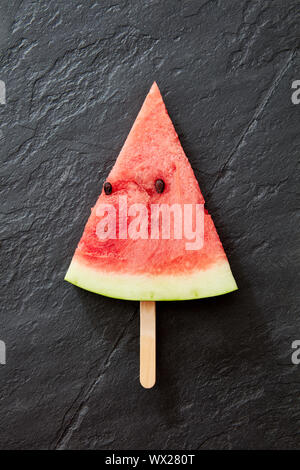 Eine Komposition von süßen Stück Wassermelone auf einem schwarzen konkreten Hintergrund. Ein Stück Wassermelone in Form eines Eis lol Stockfoto