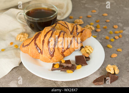 Tasse Kaffee und Schokolade Croissant mit Rosinen und Nüssen auf grauem Hintergrund. Frühstück Konzept. Stockfoto