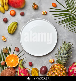 Palm Blätter, leere weiße Platte und eine Reihe von verschiedenen tropischen Früchten Mango, Passionsfrucht, Banane, Kokosnuss, Physalis, Ananas Stockfoto